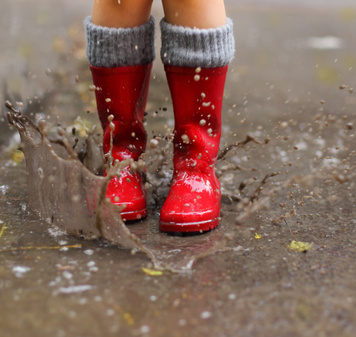 Child wearing red rain boots jumping into a puddle