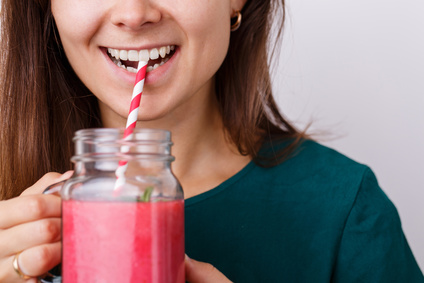 Young woman is holding tasty smoothie in glass jar with drinking straw.