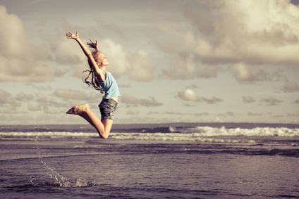 teen girl jumping on the beach at blue sea shore in summer vaca
